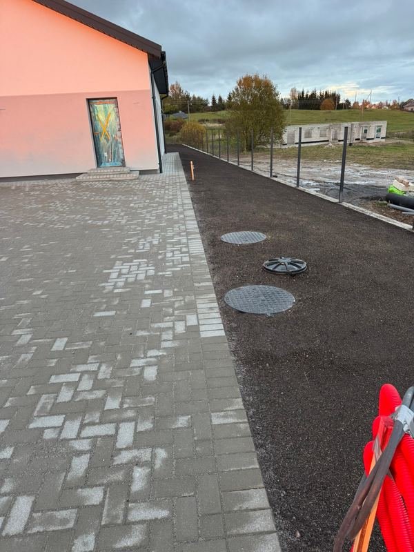 Trinkelių takas su drenažo šulinių dangčiais prie namo